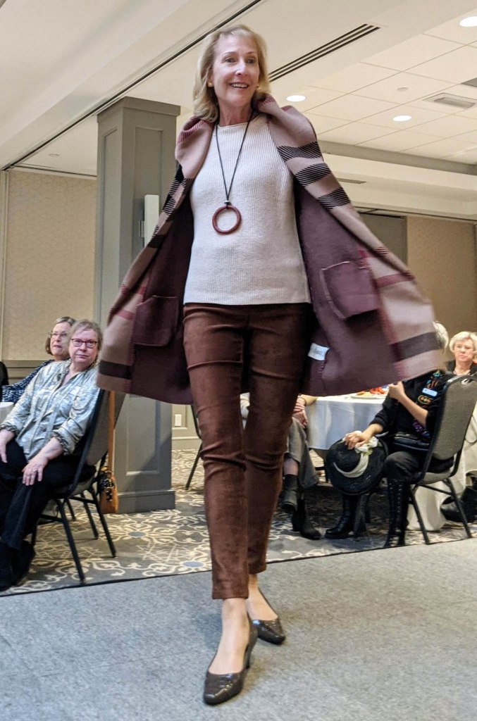 Lady in mauve with knitted jacket and white top, necklace with large ring at the end.