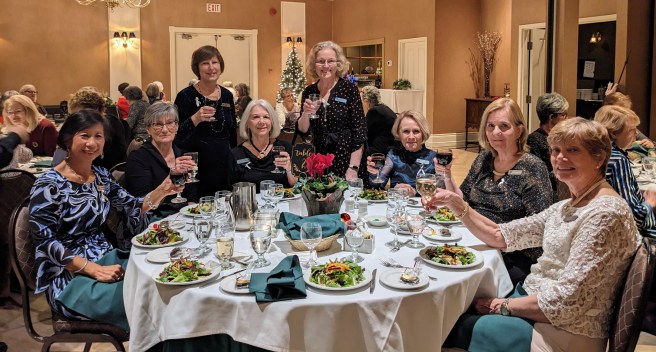 8 ladies at a circular table with drinks raised festive outfits
