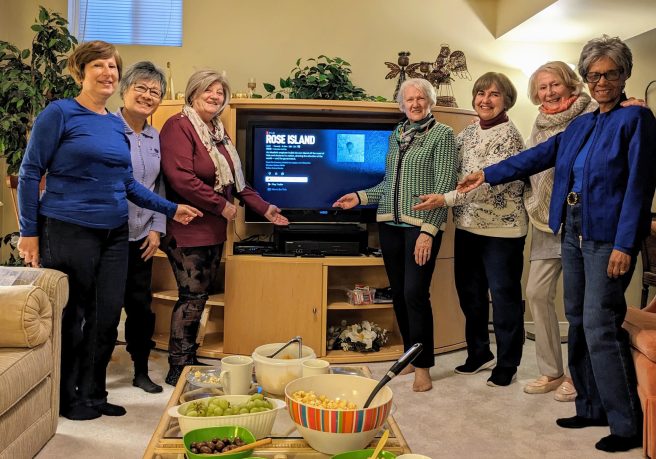Foreign Film Group 7 ladies around a flat screen tv with snacks in front